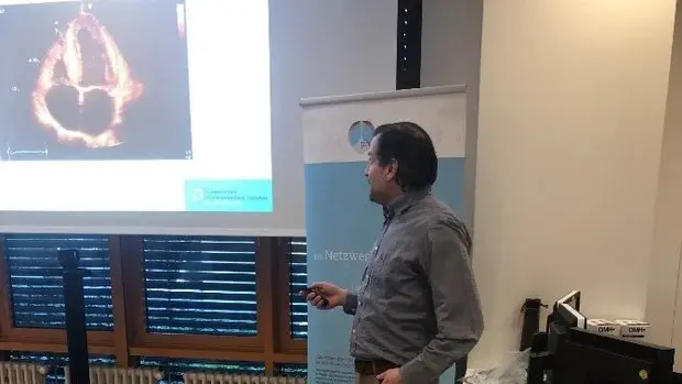 Ein Mann hält einen Vortrag und steht vor einer Projektionsleinwand, auf der ein medizinisches Bild zu sehen ist.